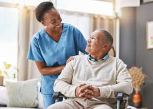 Caregiver smiling at an elderly man in a wheelchair, symbolizing compassionate elderly care.