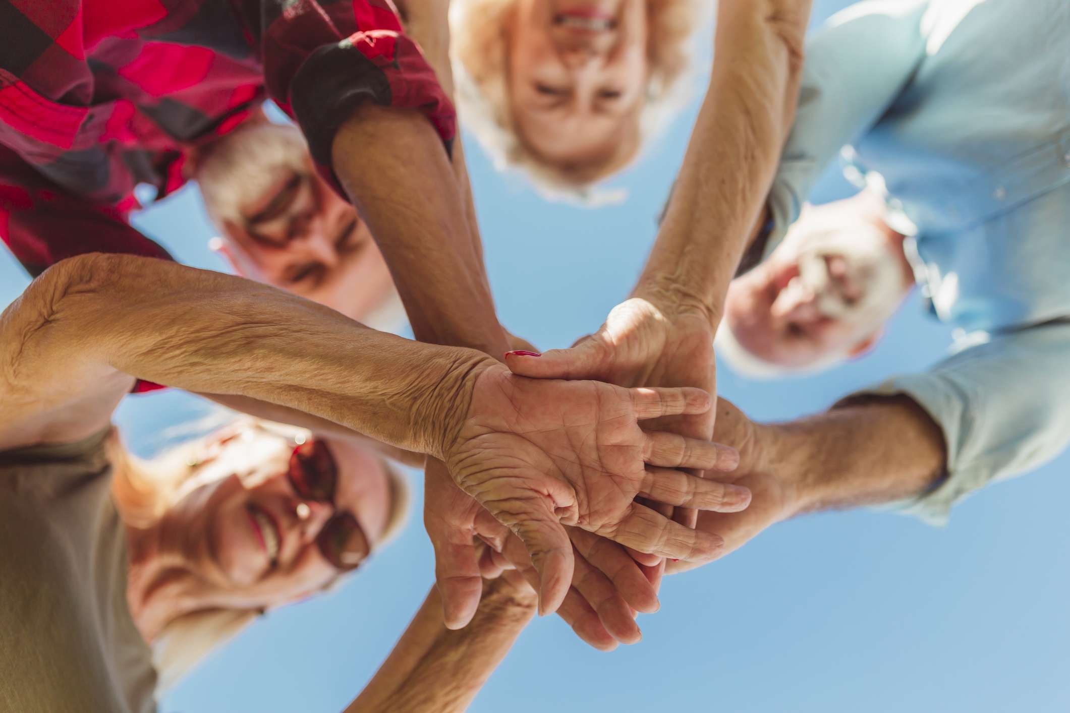 Seniors joining hands together in a circle, symbolizing community support and collaboration for health and wellness.